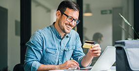 Happy guy holding credit card and looking at computer screen