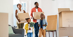 Family holding boxes moving into a new house